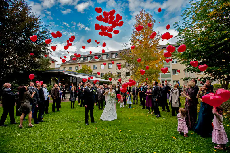 Brautpaar umkreist von den Gästen die rolle Ballone aus Herz steigen lassen. Hochzeitsfotograf UNIKATUM